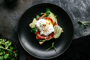 Breakfast. Sandwich with ham, poached egg, avocado and spinach in a plate on a dark background