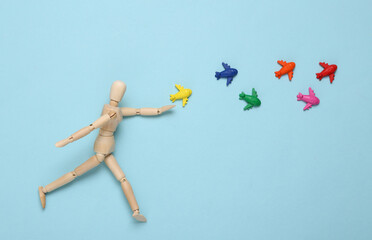 Wooden puppet playing with toy airplanes on blue background
