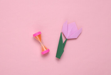 Hourglass and origami tulip on pink background