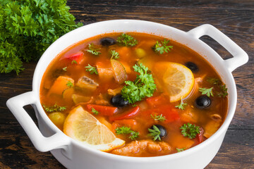 Fish soup with salmon, tilapia, red pepper, onion, carrot, lemon, green and black olives. White casserole on wooden rustic table, close-up - 411830540