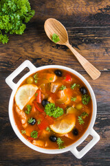  Fish soup with salmon, tilapia, red pepper, onion, carrot, lemon, green and black olives. White casserole on wooden rustic table, top view - 411830584