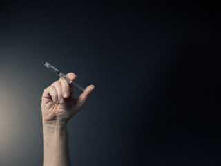 Fototapeta premium Colour image of man's hand holding syringe upwards with liquid droplet on needle point, with dramatic lighting and text space to right