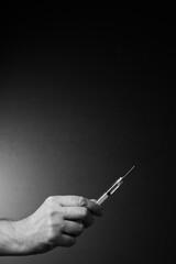 Fototapeta premium Black and white image of man's hand holding syringe upwards in fingertips with dramatic lighting and text space above