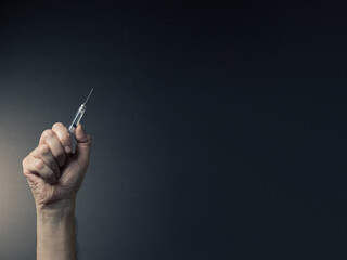 Colour image of man's clenched hand holding syringe upwards with dramatic lighting and text space to right