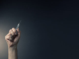 Fototapeta premium Colour image of man's clenched hand holding syringe upwards with dramatic lighting and text space to right