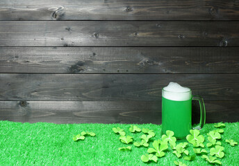 Mug of green beer on green grass with clover leaves on dark wooden planks background. Saint Patricks Day banner, poster, flyer, invitation template