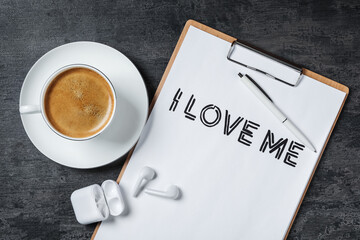 Paper with handwritten phrase I Love Me, cup of coffee and earbuds on grey stone table, flat lay