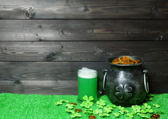Mug of green beer and cast iron pot with four-petal lucky shamrock leaf, full of leprechaun gold treasure, shamrock leaves and coins on green grass, dark wooden planks background. Saint Patricks Day