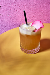 drink z limonką i płatkiem róży na żółto różowym tle. podany z ozdobną rurką. 
