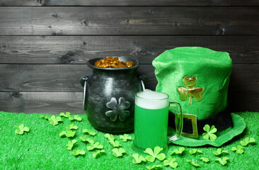 Mug of green beer, cast iron pot with treasure and leprehaun hat, clover leaves and coins on green grass, dark wooden planks background. Saint Patricks Day banner, poster, flyer, invitation template