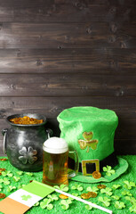 Mug of beer and leprehaun hat, cast iron pot with gold treasure, shamrock leaves, flag of Ireland and coins on green grass, wooden background. Saint Patricks Day banner, poster, flyer, invitation