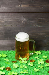 Mug of beer, shamrock leaves and leprechaun gold coins on green grass, dark wooden planks background. Saint Patricks Day banner, poster, flyer, invitation template