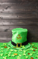 Green leprechaun hat with gold clover leaf, shamrock leaves and leprechaun gold coins on green grass, dark wooden planks background. Saint Patricks Day banner, poster, flyer, invitation template