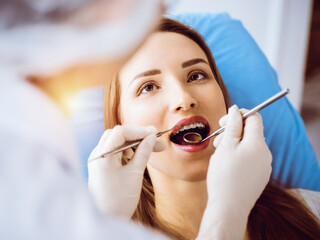 Smiling young woman with orthodontic brackets examined by dentist in sunny dental clinic. Healthy teeth and medicine concept