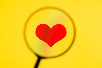 Red heart on yellow screen through magnifying glass.