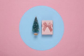 Mini Christmas tree and gift box on a blue-pink round background. Minimalism