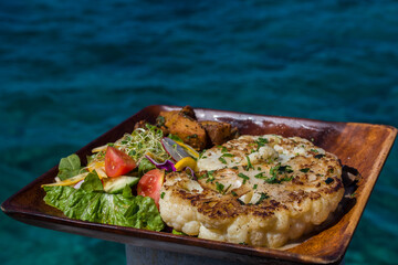 vegan cauliflower steak served outside on a wooden plate with green salad and sauteed potatoes