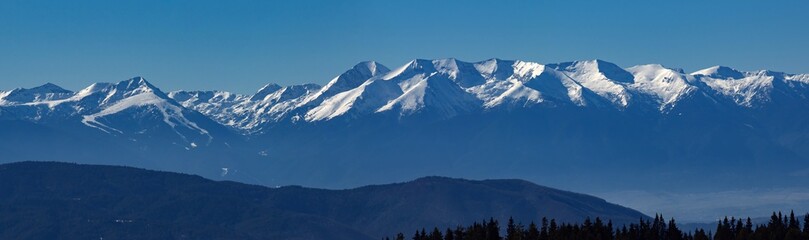 Beautiful winter panoramic mountain landscape. The white snowy peaks of Pirin Mountains, viewed from The Rila Mountains in Bulgaria, blue sky. Snowy weather conditions for winter sports and tourism.