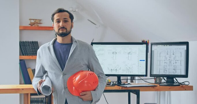 Engineer on the background of an office in a working environment point a man stands with a roll of drawings and a construction helmet in his hand. A professionalism as a guarantee of quality work