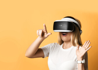 Portrait of surprised excited woman in white t-shirt using VR glasses exploring augmented reality pressing virtual button with finger. Modern cyber technologies concept