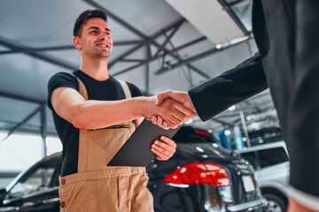 Businessman customer shaking hands with the mechanic in the auto repair shop.