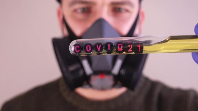 Caucasian Male Scientist Wearing Gas Mask and Blue Latex Gloves while Examining Test Tube With Covid 21 Sample
