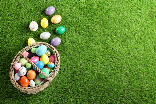 Wicker basket with Easter eggs on green grass, flat lay. Space for text