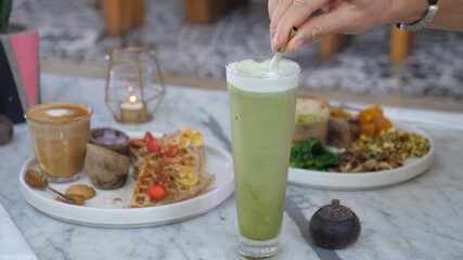 Hand stirring matcha ice latte in a glass with a metal stoke.Healthy Vegan breakfast for two.