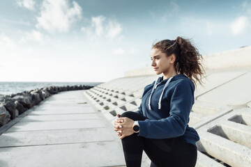 Curly sports woman in sportswear doing body warming up before training on urban beach. Healthy lifestyle