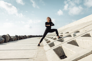 Outdoor workout concept. Fit slim woman with curly hair stretches or warms up on an urban...
