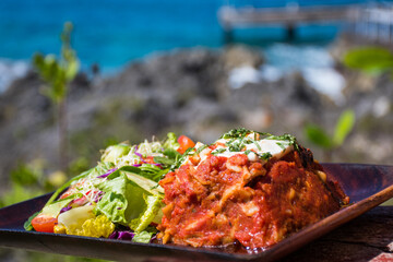 vegetarian lasagne served with green salad outside on a wooden plate