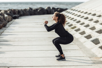 Outdoor workout concept. Fit slim woman with curly hair crouches on an urban embankment with concrete slabs