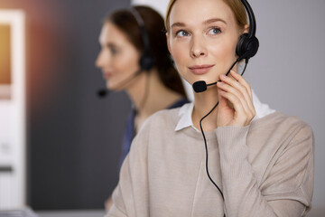 Businesswoman talking by headset while sitting in sunny office. Call center and diverse people...