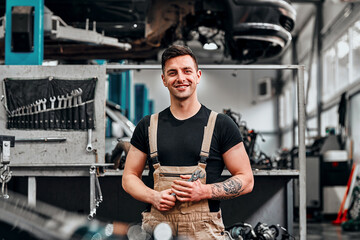 Happy smiling auto mechanic man with wrenches at the workshop.