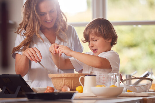 Mother And Son In Pyjamas Making Pancakes In Kitchen At Home Following Recipe On Digital Tablet