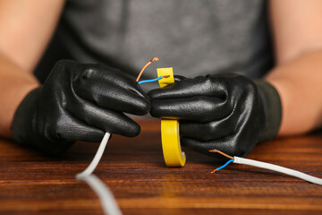 Bare wires are insulated with duct tape by a man in work gloves. Connection of two wires.