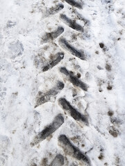 Imprint of tractor or snowblower tire on road surface covered with dirty melting snow. Abstract vertical oblique lines background.
