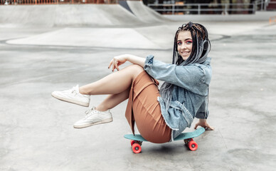 Extraordinary female millennial skater with colorful makeup, African braids sits on penny board at skate park. Youth, lifestyle concept © splitov27