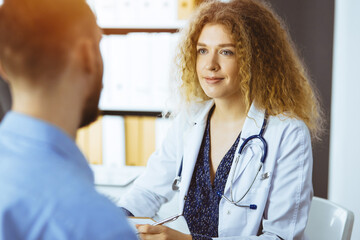 Female doctor and male patient discussing current health examination while sitting in sunny clinic. Medicine concept