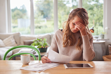 Worried Woman With Digital Tablet Sitting At Table At Home Reviewing Domestic Finances - obrazy, fototapety, plakaty