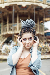 Fototapeta premium Extraordinary woman with African braids and flamboyant makeup spends time in an amusement park