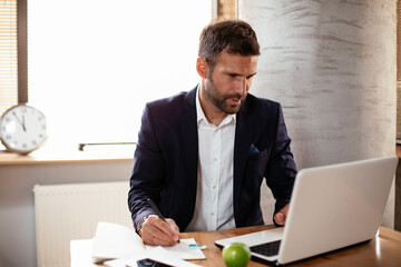 Young businessman using laptop in his office. Businessman taking a notes while working on laptop..