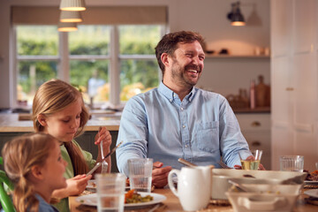 Father And Children Sitting Around Table At Home Enjoying Meal Together