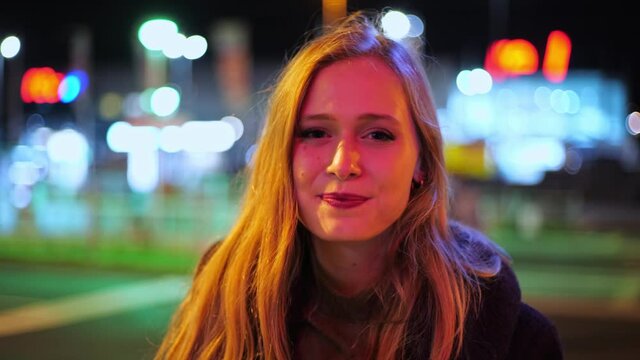 [4k] young blonde woman putting of ffp2 mask in colourfull big city light at night