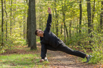 Active sport man trains warm-up exercises or stretching in the autumn forest. Healthy lifestyle. Outdoor workout