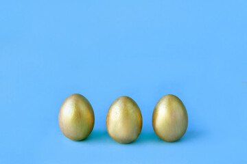 Easter eggs on blue background. Three golden eggs. Minimal style. Easter decorations.