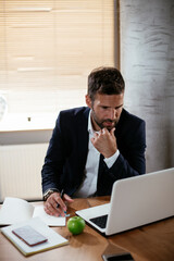 Young businessman using laptop in his office. Businessman taking a notes while working on laptop..