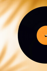 Flat lay of LP vinyl record on a yellow or orange background with tropical palm leaves shadow.  Old vintage record. Hipster style