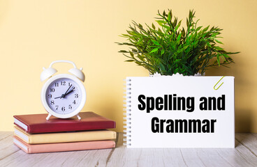 SPELLING AND GRAMMAR is written in a notebook next to a green plant and a white alarm clock, which...