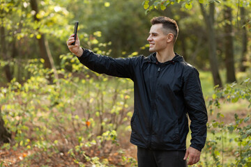 Handsome man taking selfie on phone in autumn forest